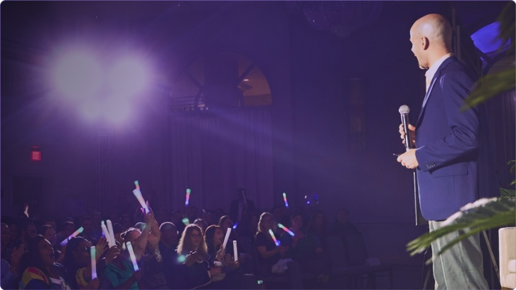 A speaker holding a microphone on stage in front of a crowd at a Cotiviti Client Conference